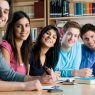 Happy group of young students studying together in a college library and looking at camera smiling